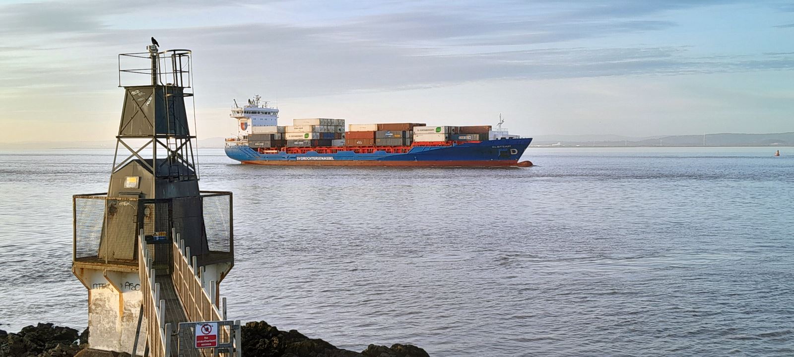 A huge container ship passing the tiny Portishead Point Lighthouse in North Somerset